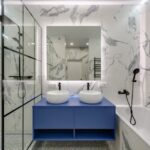 Modern bathroom interior featuring marble walls, dual sinks, and a glass shower.